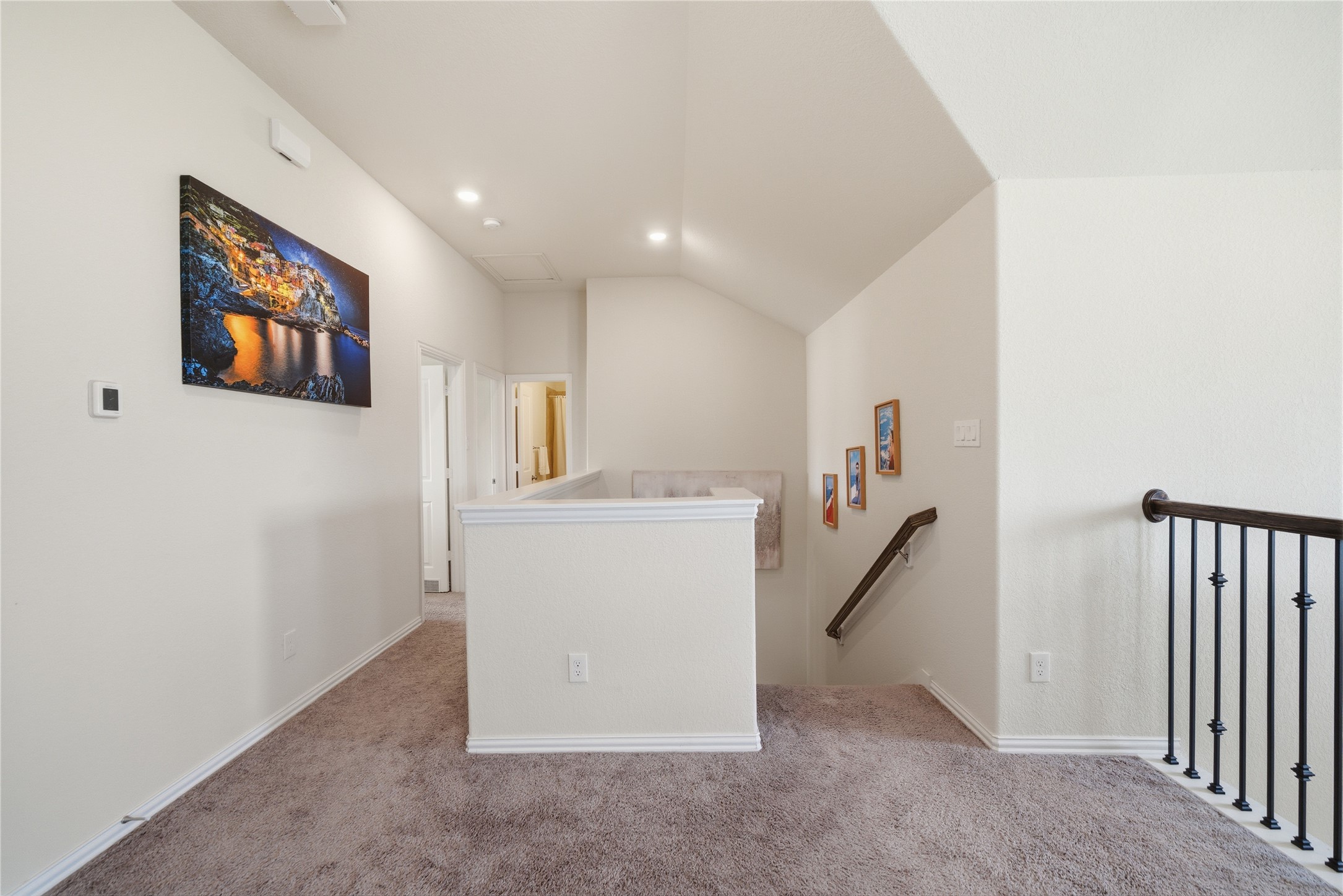 4335 Tawny Timber Drive Spring, TX 77386 - Photo 22 of 42 This photo shows a bright, carpeted upstairs landing area with recessed lighting. It features a partial open railing with wooden handrails and decorative iron spindles. Walls are adorned with framed artwork, adding a personal touch. The space leads to additional rooms, creating a cozy and functional transition area in the home.