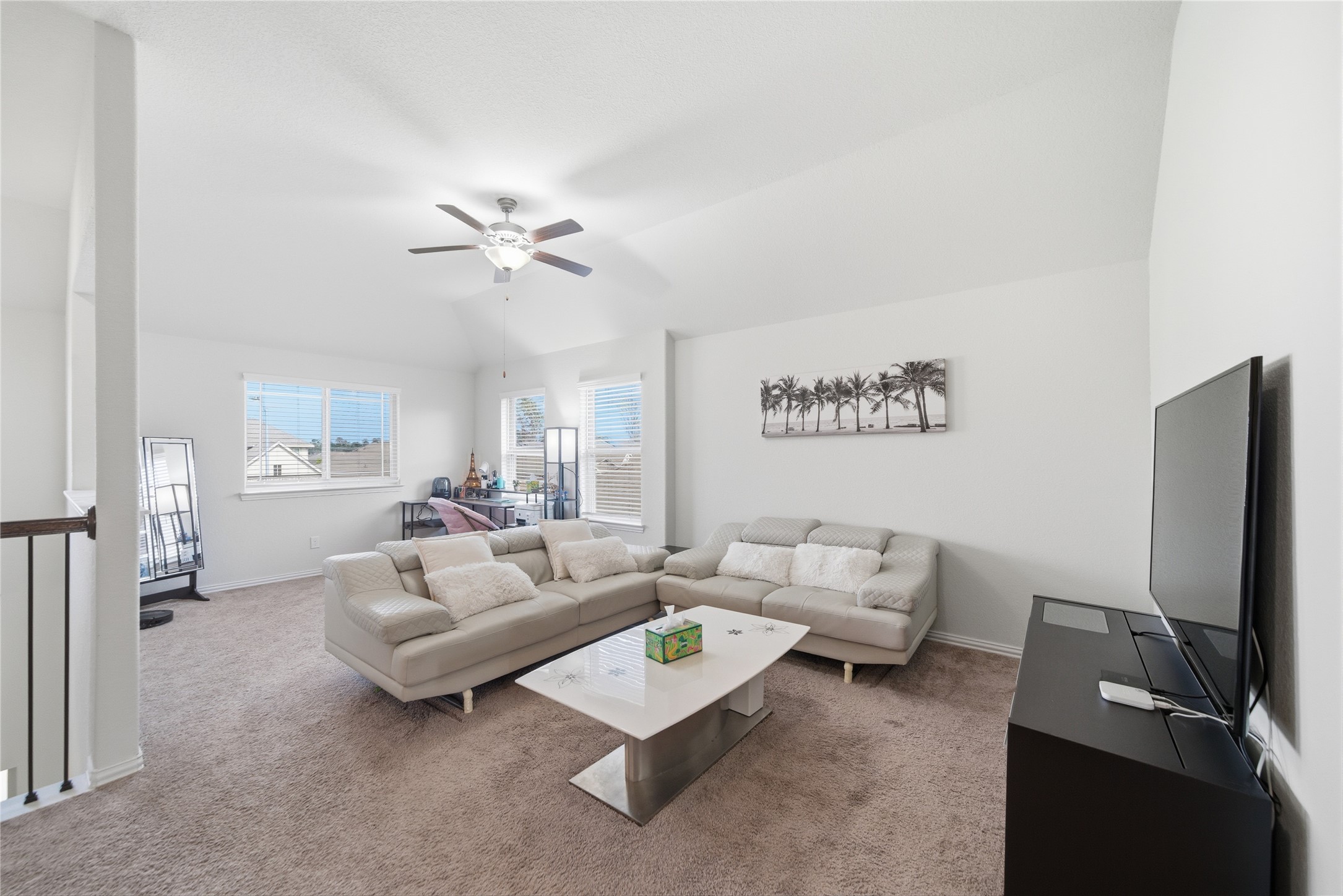 4335 Tawny Timber Drive Spring, TX 77386 - Photo 26 of 42 Bright and airy living room featuring plush carpeting, a modern ceiling fan, and ample natural light from multiple windows. The space is furnished with comfortable sofas, a sleek coffee table, and a large TV, offering a cozy and inviting atmosphere.