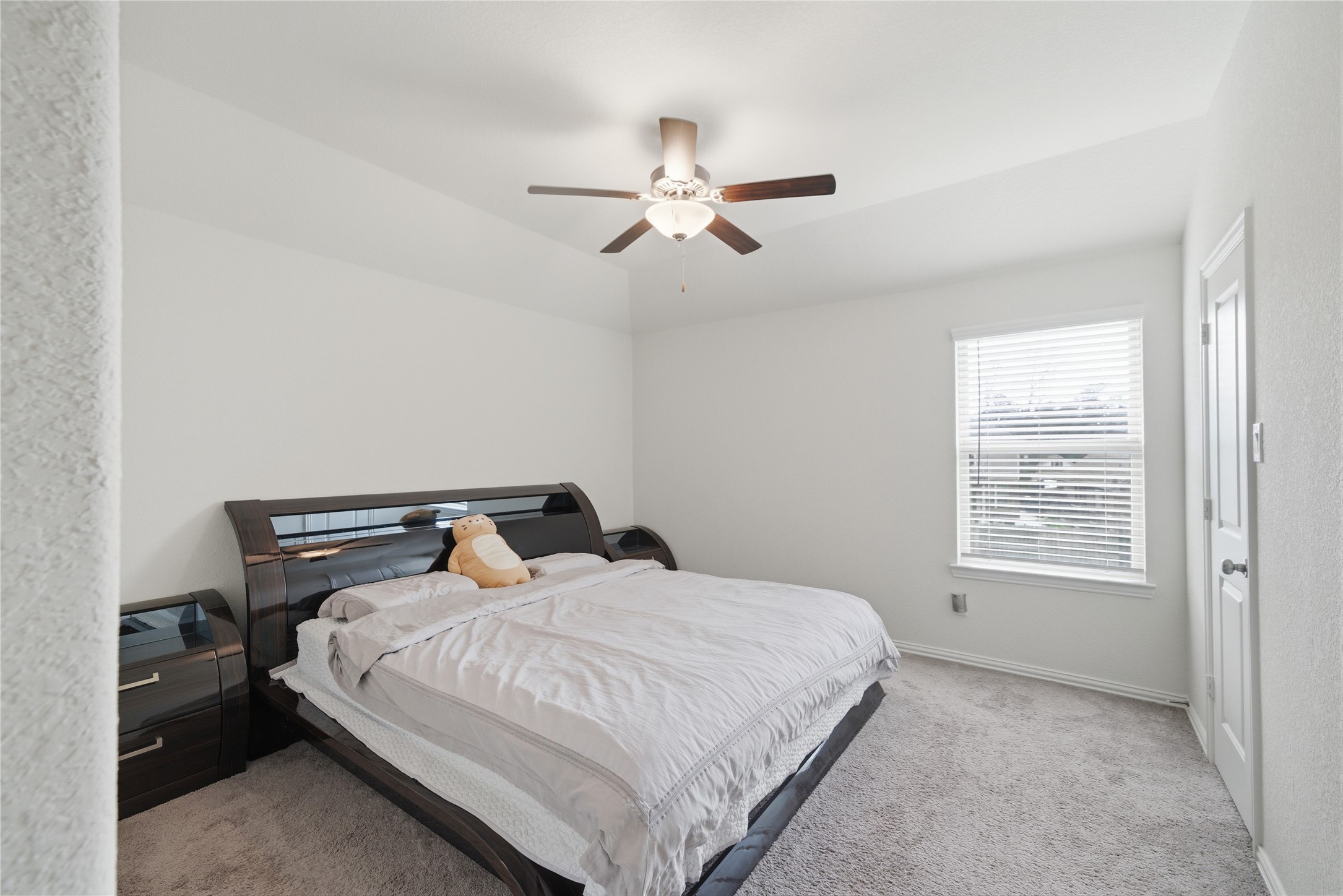4335 Tawny Timber Drive Spring, TX 77386 - Photo 28 of 42 This is a bright, cozy bedroom featuring a large bed with a modern headboard, a ceiling fan, and a window providing natural light. The neutral walls and carpet create a clean and inviting atmosphere.