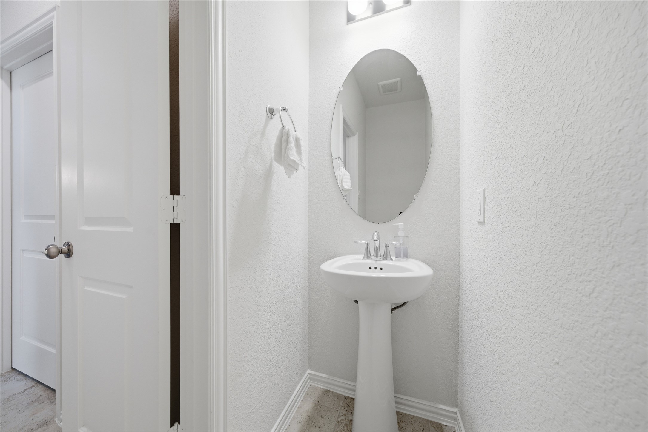 4335 Tawny Timber Drive Spring, TX 77386 - Photo 35 of 42 This photo shows a compact, bright bathroom featuring a pedestal sink with an oval mirror above it. The walls are light-colored, and there's a towel holder nearby, creating a clean and simple look.