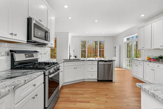 a kitchen with stainless steel appliances granite countertop a stove top oven a sink dishwasher a refrigerator and a dining table with wooden floor