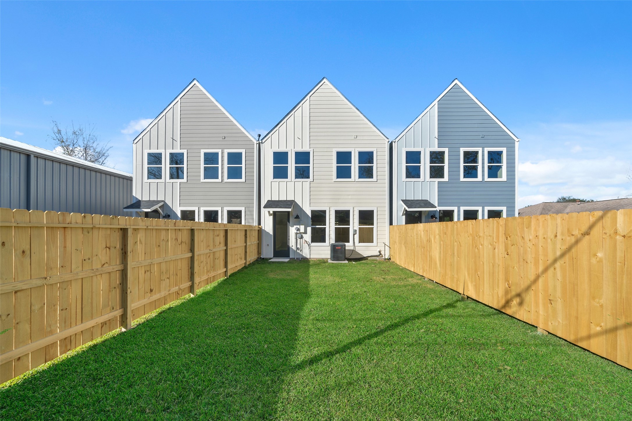 3422 Elser Street Houston, TX 77009 - Photo 18 of 26 This photo shows a modern townhouse with three distinct sections, featuring a symmetrical design and large windows. It's surrounded by a wooden fence and has a well-maintained grassy yard, offering privacy and outdoor space.