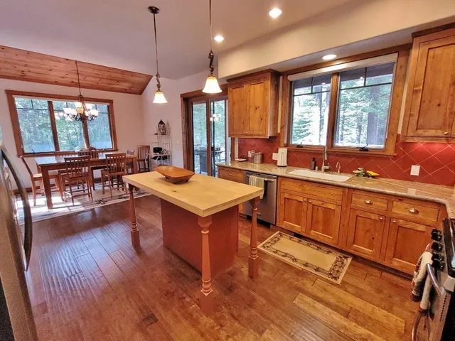 a large kitchen with kitchen island wooden floors wooden cabinets a sink a window and appliances