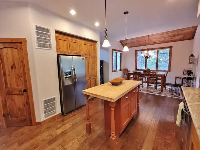 a kitchen with stainless steel appliances granite countertop a refrigerator a sink dishwasher a stove and a dining table with wooden floor