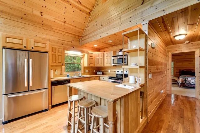 a kitchen with stainless steel appliances a stove a refrigerator a oven a sink a dining table and chairs with wooden floor