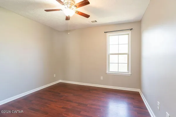 an empty room with wooden floor chandelier fan and windows