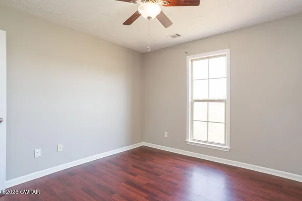 an empty room with wooden floor chandelier fan and windows