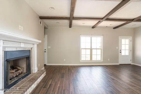 a view of an empty room with wooden floor fireplace and a window