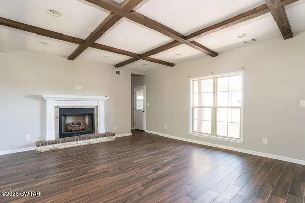 a view of an empty room with wooden floor fireplace and a window