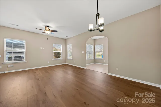 an empty room with wooden floor chandelier and windows