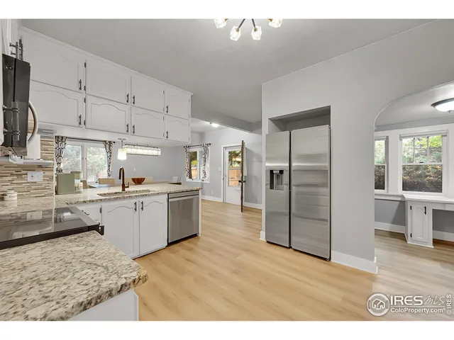 a kitchen with stainless steel appliances kitchen island granite countertop a refrigerator oven a sink dishwasher and white cabinets with wooden floor