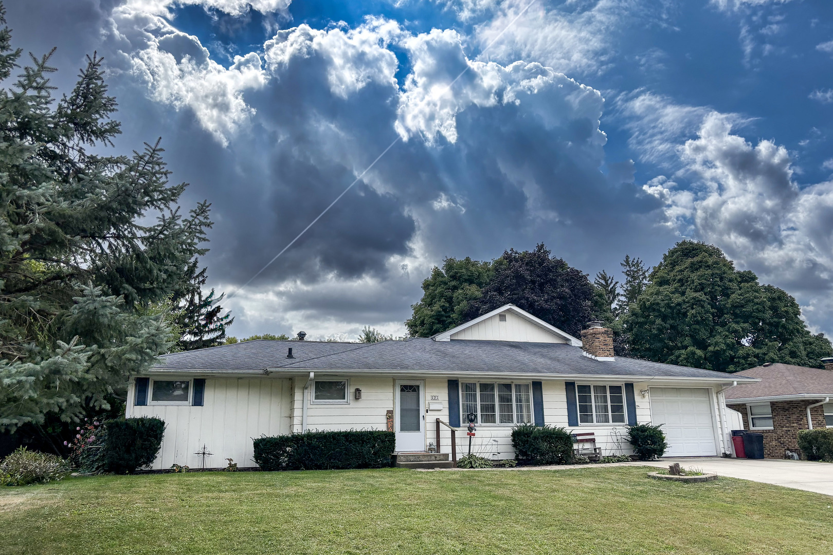 a view of a white house with a yard plants and large tree