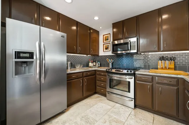 a kitchen with stainless steel appliances granite countertop a refrigerator a sink a stove and oven