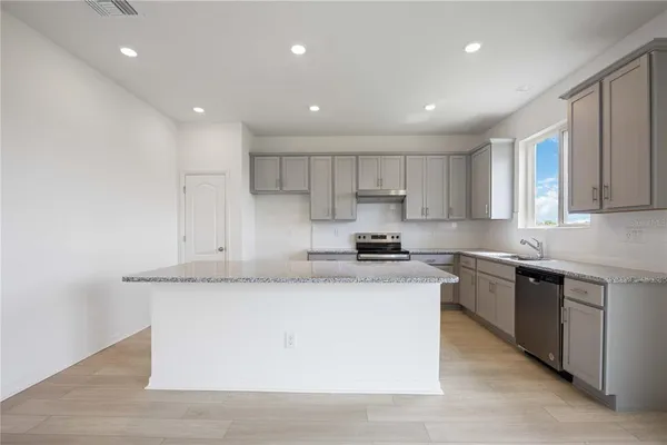 a large kitchen with stainless steel appliances granite countertop a stove a sink a refrigerator and white cabinets