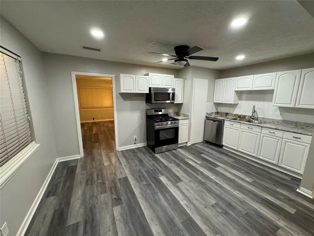 a kitchen with granite countertop a refrigerator oven a sink dishwasher and white cabinets with wooden floor