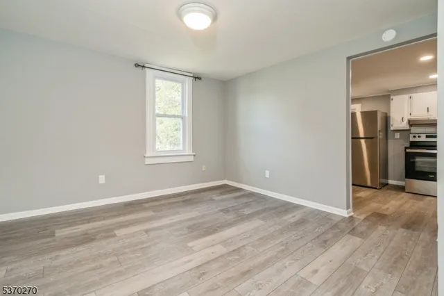 an empty room with wooden floor kitchen view and windows