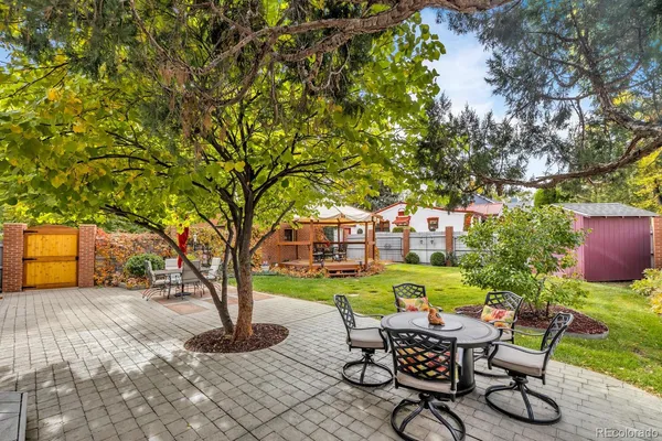 a view of a backyard with table and chairs potted plants and a large tree
