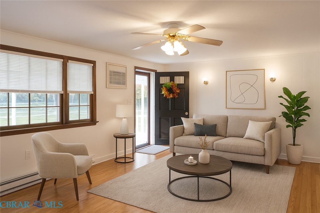 Living room with light wood finished floors, a baseboard radiator, a ceiling fan, and ornamental molding