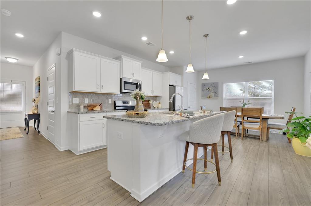 803 Dundee Way Cartersville, GA 30121 - Photo 5 of 37 a kitchen with stainless steel appliances granite countertop a stove a sink a refrigerator a microwave oven with a dining table and chairs with wooden floor