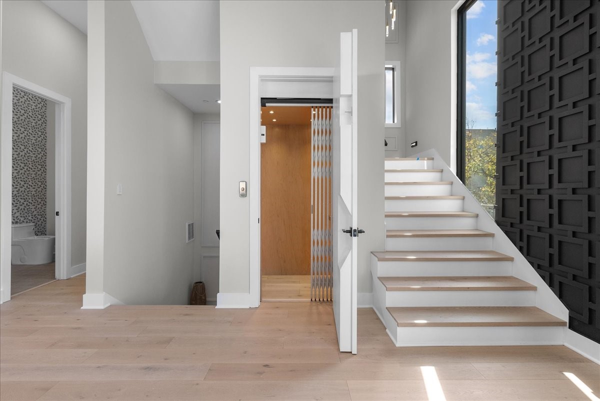 516 Reinerman Street Houston, TX 77007 - Photo 37 of 42 This modern home features a light-filled entryway with a sleek staircase and an elevator. A stylish black accent wall adds depth, while hardwood floors and neutral walls create a warm, inviting atmosphere. A bathroom is visible to the left, offering convenience.