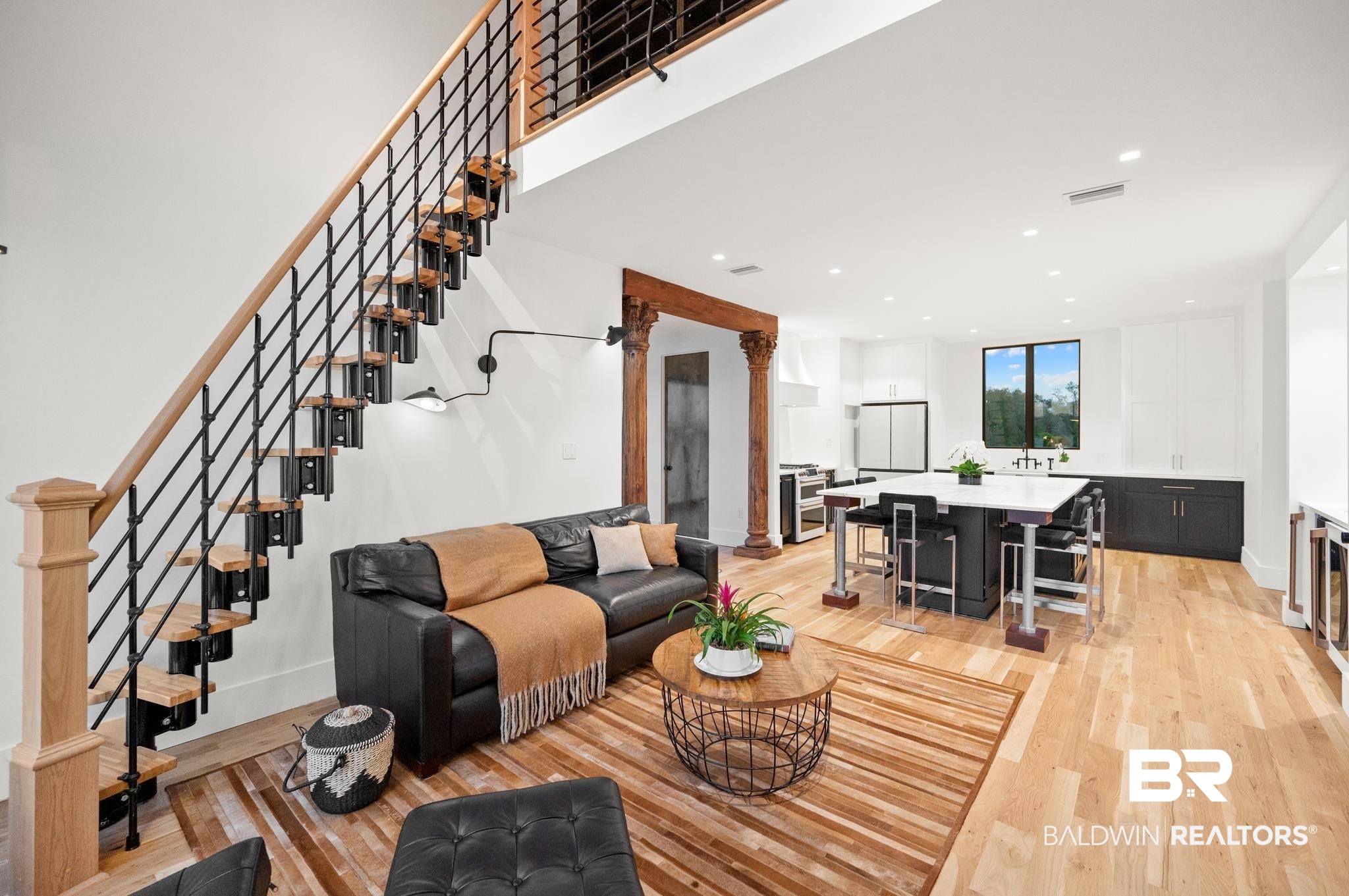 33349 River Road Orange Beach, AL 36561 - Photo 9 of 61 Open-concept interior featuring light wood-finish flooring, a contemporary staircase with black metal balusters and wood handrails, a spacious kitchen island with seating, recessed lighting, and a large window with outdoor scenery