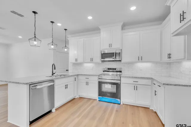 a kitchen with stainless steel appliances granite countertop a sink a stove a refrigerator and white cabinets with wooden floor