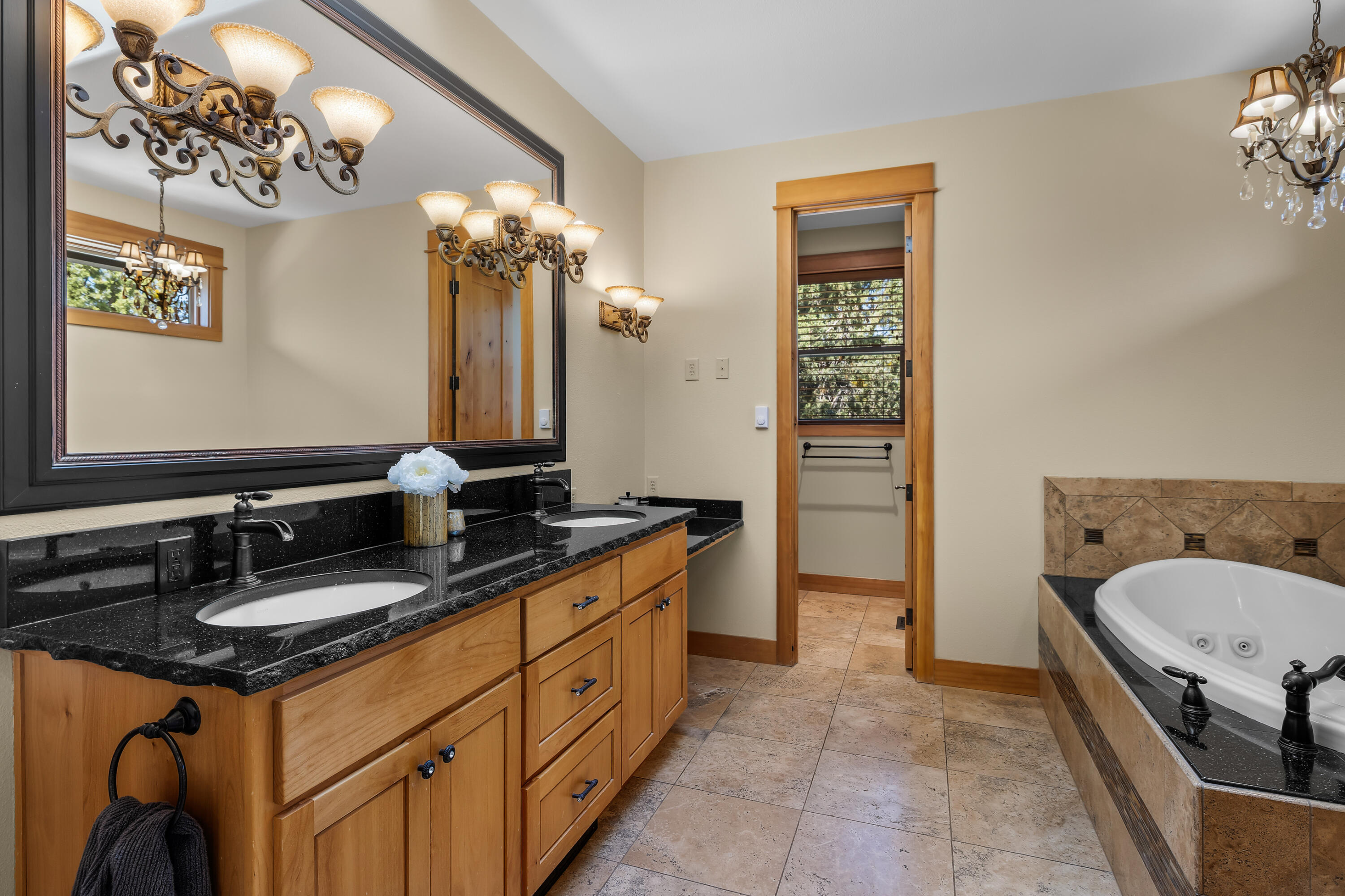 64145 Hunnell Road Bend, OR 97703 - Photo 20 of 65 The primary bath features a spacious dual vanity, warm cabinetry, stone counters, vaulted ceiling detail and a bathtub positioned for a relaxed retreat-like feel.