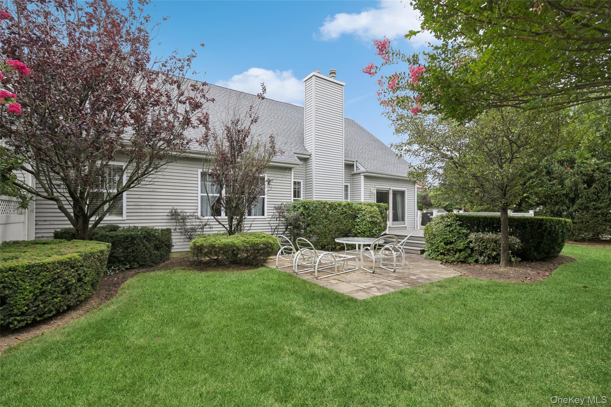 103 Rivendell Court Melville, NY 11747 - Photo 35 of 47 Back of house featuring a patio area, a shingled roof, a yard, and a chimney