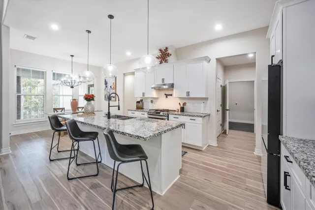 a kitchen with stainless steel appliances granite countertop a kitchen island a stove a refrigerator a sink a dining table and chairs with wooden floor