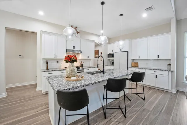 a kitchen with kitchen island granite countertop a dining table chairs and white cabinets