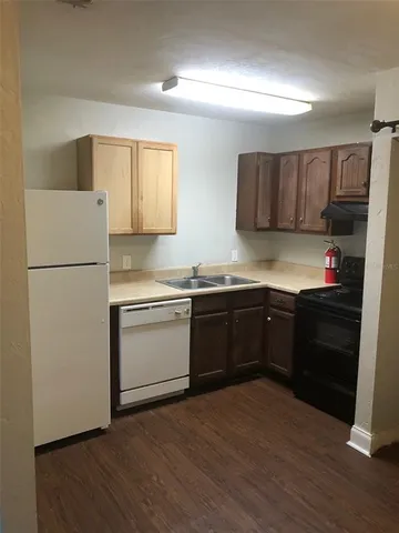 an empty room with wooden floor and way to kitchen