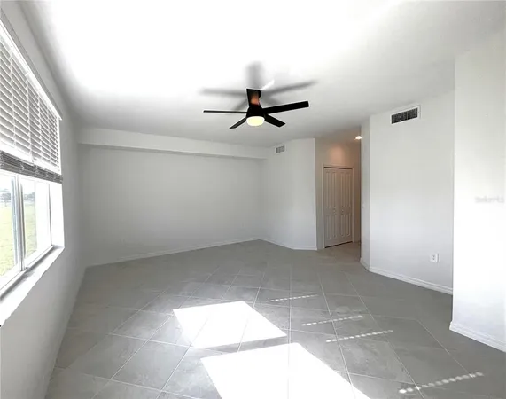 an empty room with chandelier fan and windows