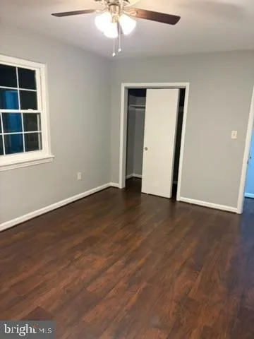 a view of an empty room with wooden floor and fan