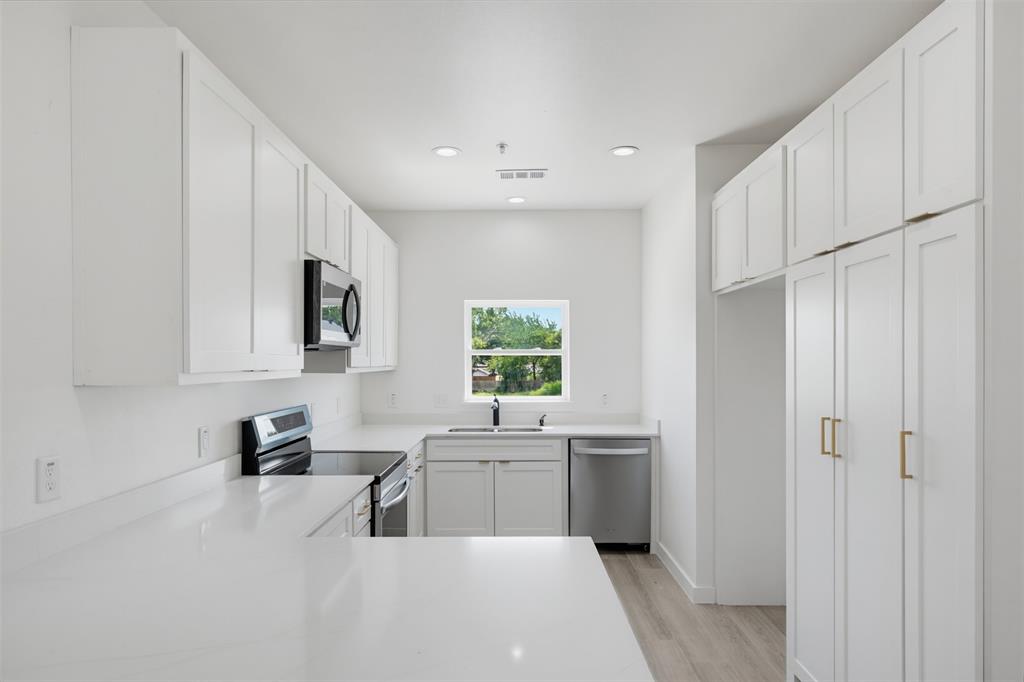 516 South O Connor Road Irving, TX 75060 - Photo 2 of 23 Modern kitchen featuring white shaker cabinetry, stainless steel appliances, light-toned countertops, a built-in microwave, and wood-finish flooring