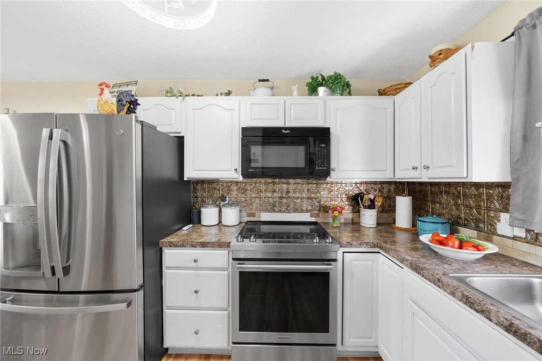 9208 Thorpe Road Berlin Heights, OH 44814 - Photo 11 of 47 Kitchen featuring appliances with stainless steel finishes, decorative backsplash, white cabinets, dark countertops, and a textured ceiling