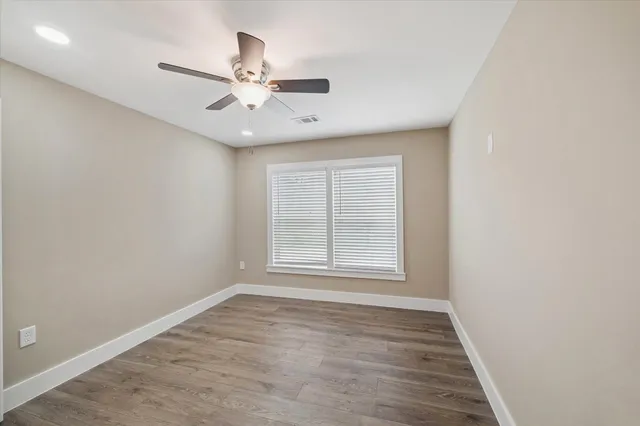 an empty room with wooden floor fan and windows