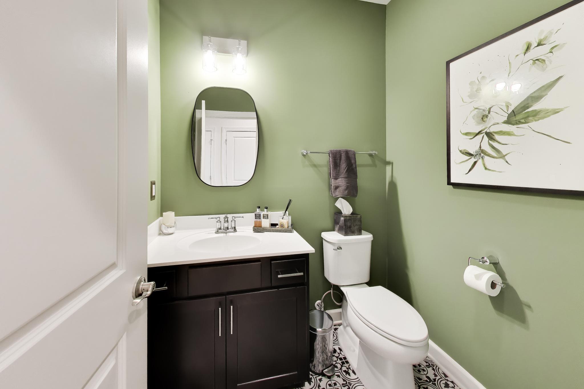 2730 Harbor Court Delavan, WI 53115 - Photo 23 of 47 Main-level powder room with green accent walls, dark vanity, framed mirror, and patterned tile floor.