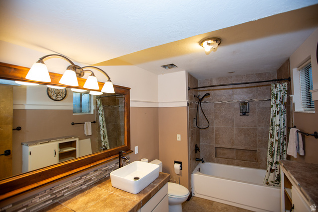 1500 Sumac Drive Logan, UT 84321 - Photo 34 of 42 Full bathroom featuring a built-in tub with tile surround, a vessel sink on a tiled countertop, a wooden framed mirror, and a four-light vanity fixture
