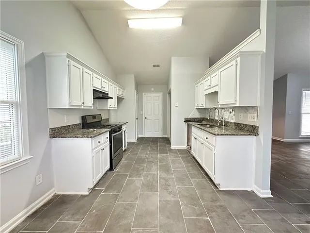 a large kitchen with kitchen island granite countertop a stove a sink a refrigerator and white cabinets