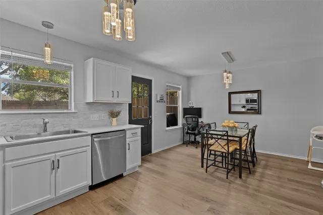 a kitchen with stainless steel appliances granite countertop a dining table chairs a sink and dishwasher a refrigerator with wooden floor