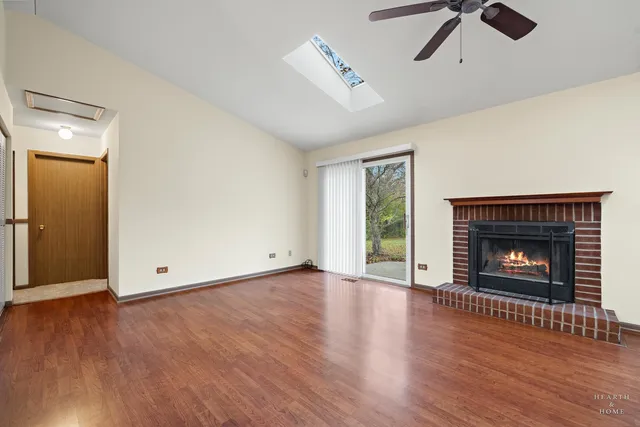 an empty room with windows a fireplace a ceiling fan and wooden floor