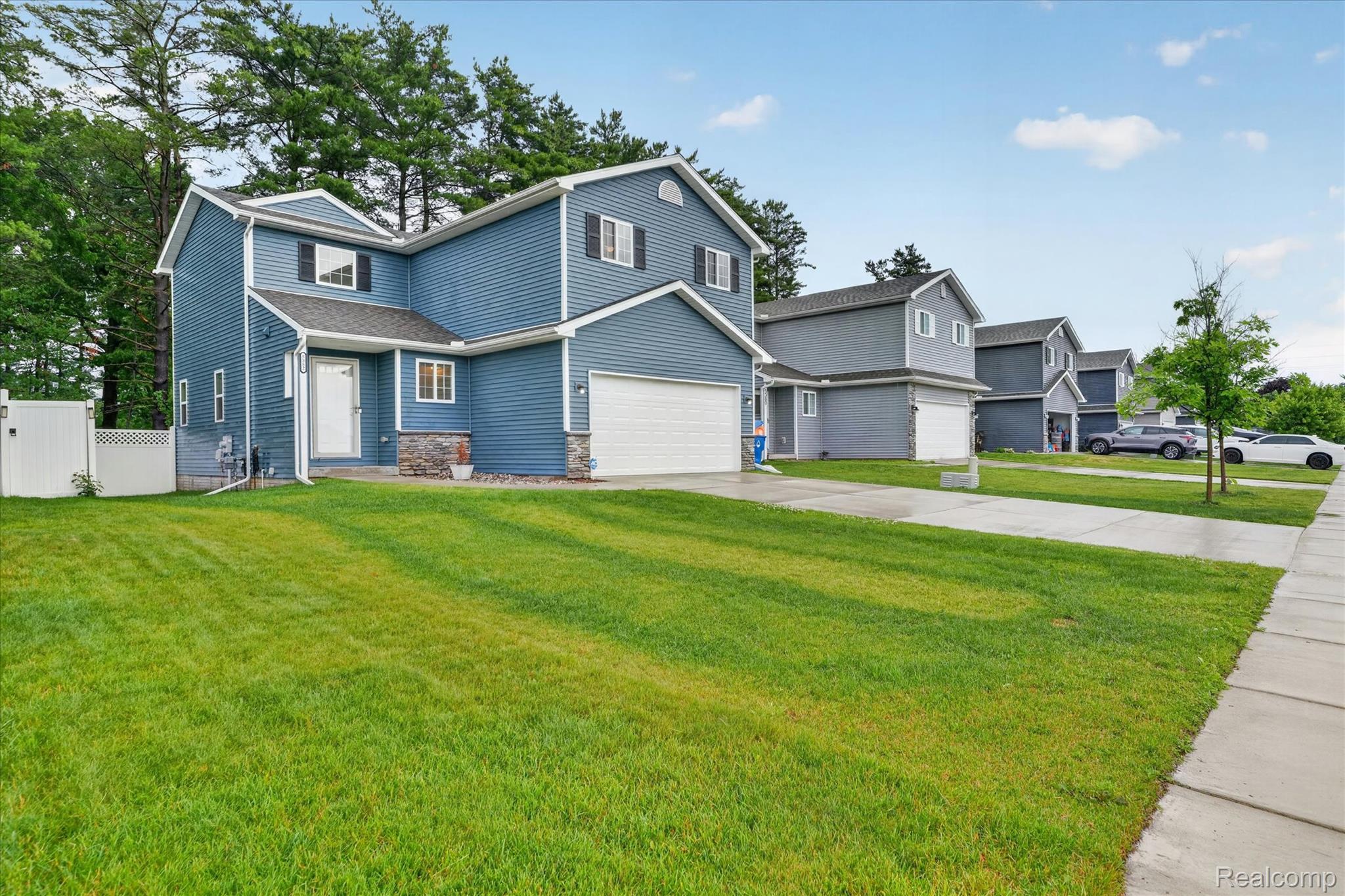 5382 Rural Terrace Waterford, MI 48329 - Photo 2 of 35 Blue siding exterior with stone accents, featuring a two-car garage, white front entry door, and a white picket fence