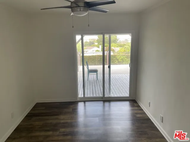 a view of an empty room with wooden floor and fan