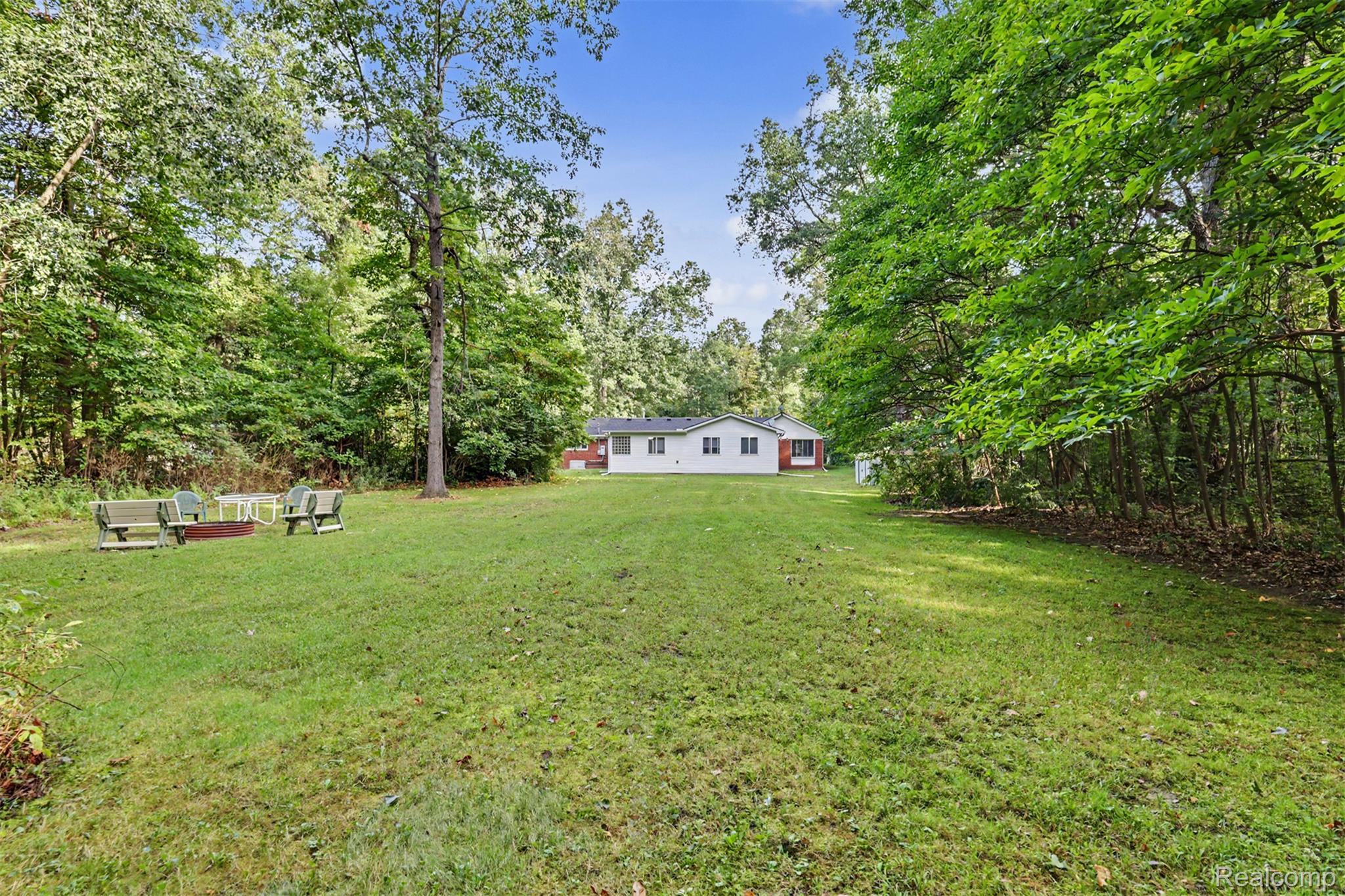 45223 Wear Road Belleville, MI 48111 - Photo 46 of 60 Expansive green lawn surrounded by mature trees, featuring a detached single-story residence with white siding and a red brick foundation