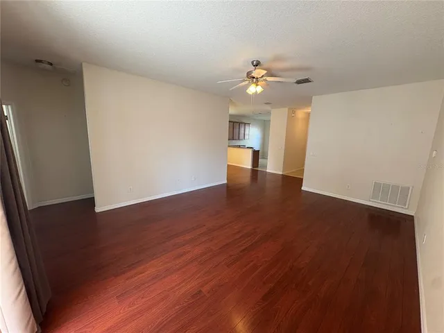 an empty room with wooden floor chandelier fan and windows