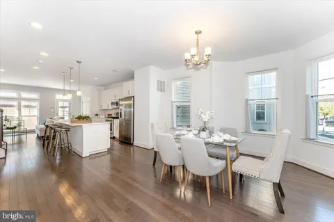 a kitchen with stainless steel appliances granite countertop a stove a refrigerator a kitchen island a dining table and chairs with wooden floor