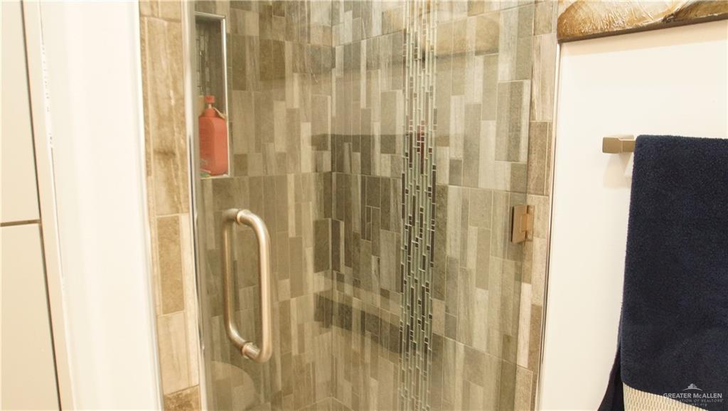 414 Ric Mar Street Edinburg, TX 78541 - Photo 33 of 36 Shower enclosure featuring glass door with brushed nickel hardware, mosaic tile accent, recessed shower niche, and wood-look wall tiling
