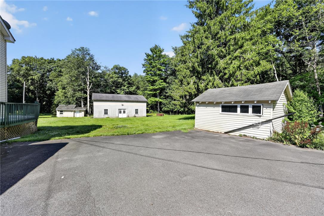 2882 Locust Ridge Road Pocono Lake, PA 18347 - Photo 13 of 45 A spacious asphalt driveway leads to a secluded property featuring several outbuildings nestled amongst mature trees and green expanses.