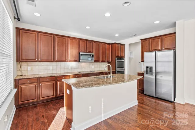 a kitchen with stainless steel appliances granite countertop a refrigerator a sink a stove a microwave and with wooden floors