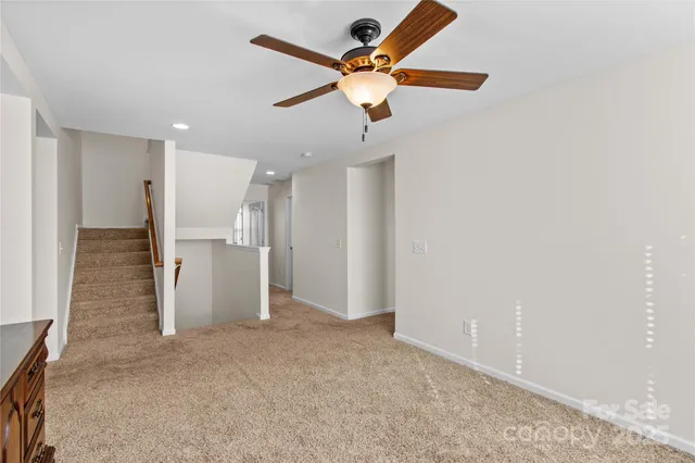 an empty room with a ceiling fan and kitchen view
